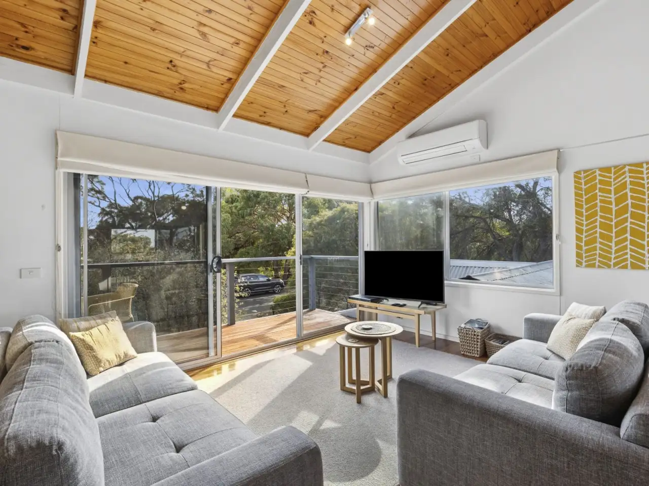 Living room with sofas, television and tall windows looking into the trees